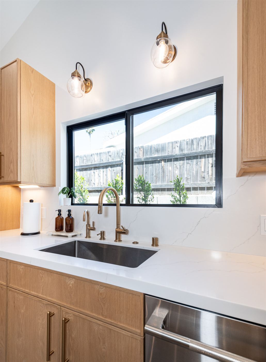 Kitchen with light wood cabinets, brass faucet and stainless sink